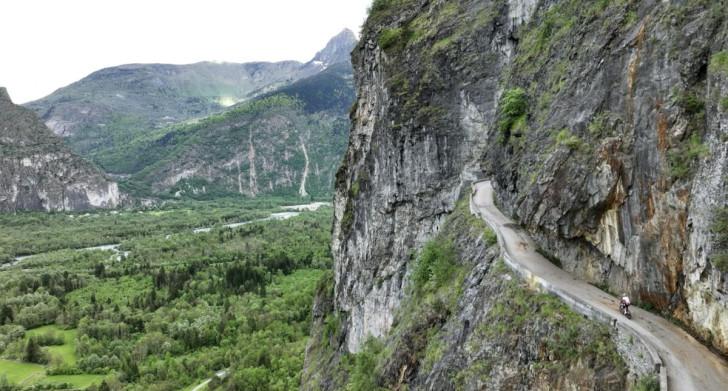 Sur la droite, on aperçoit une route à flanc de falaise. En contrebas à gauche la vallée serpentée par une rivière.